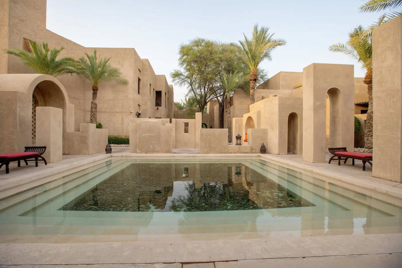A shaded sand-stone courtyard with arches, palms and a reflecting pool