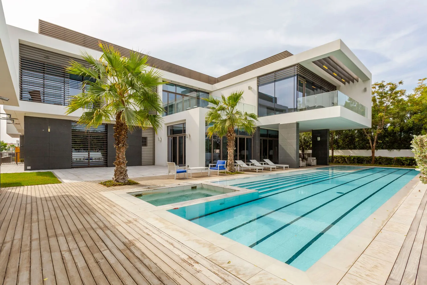 A modern two-storey villa with palms and a pool deck under a blue sky